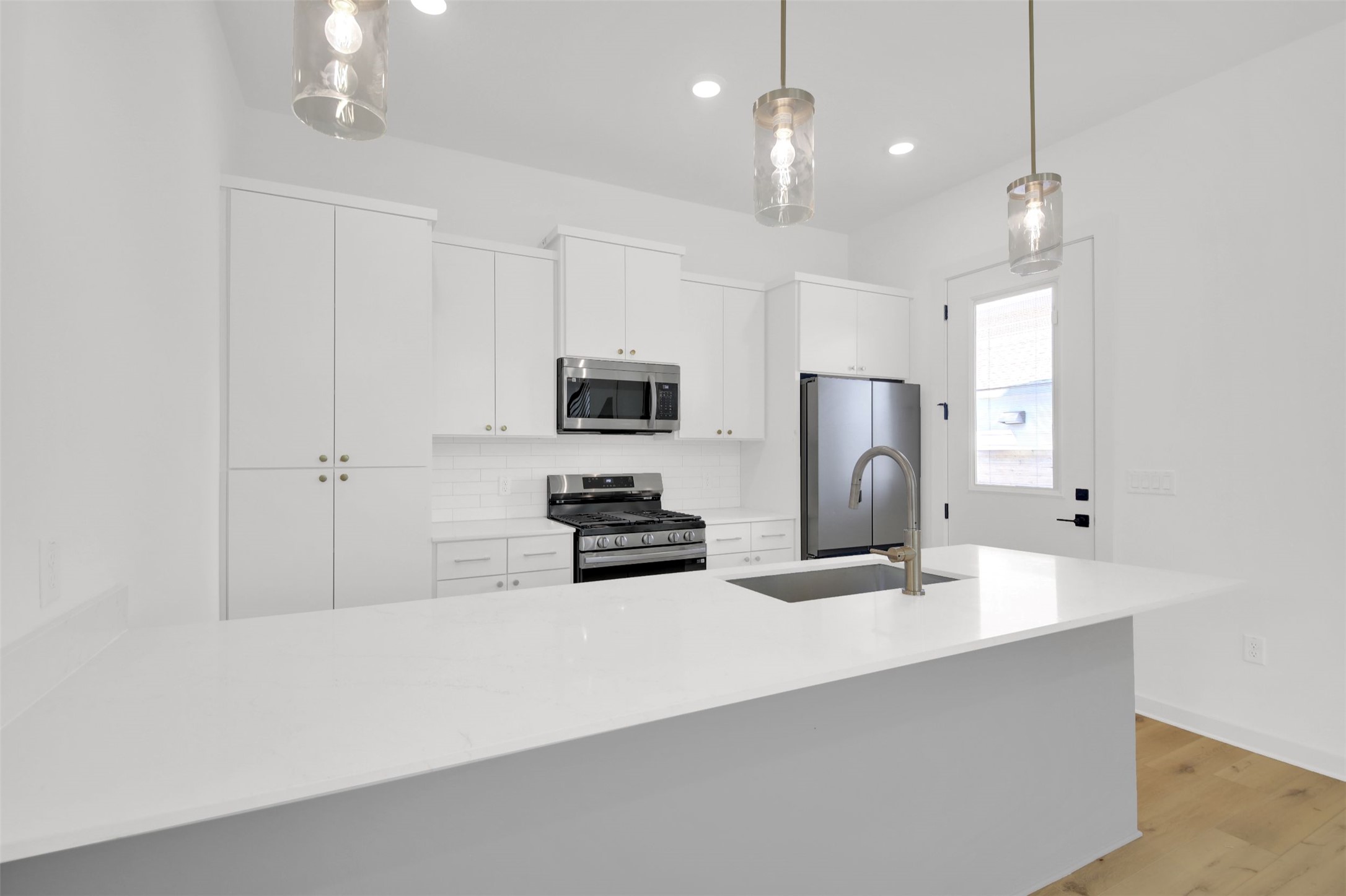 7208 Providence Avenue, Unit 1 Austin, TX 78752 - Photo 8 of 26 Well-appointed kitchen featuring a large island with a sink and faucet, white cabinetry, a stainless steel refrigerator, and a white subway tile backsplash