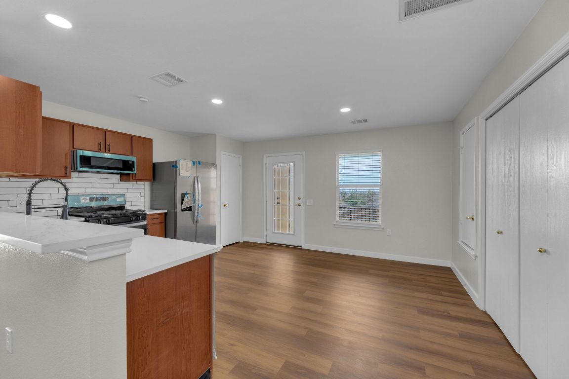 11617 Briarcreek Loop Manor, TX 78653 - Photo 8 of 37 Kitchen featuring tasteful backsplash, appliances with stainless steel finishes, brown cabinetry, dark wood finished floors, and recessed lighting