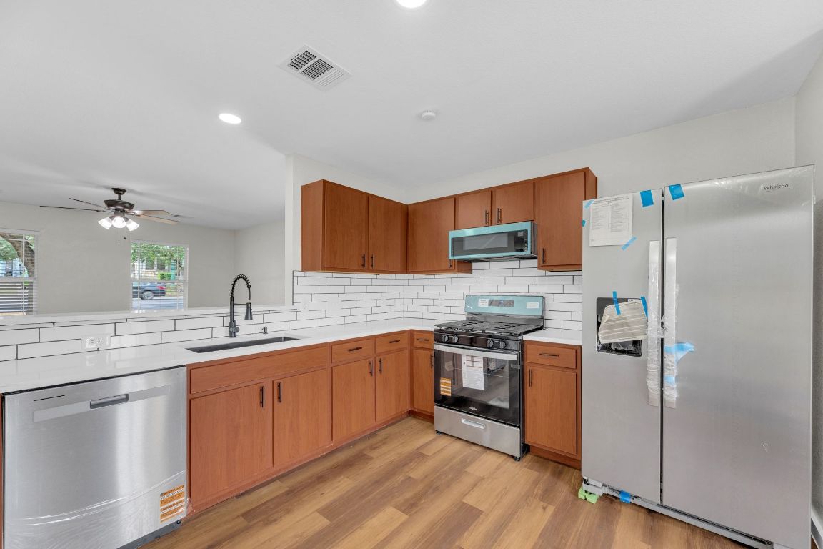 11617 Briarcreek Loop Manor, TX 78653 - Photo 9 of 37 Kitchen featuring appliances with stainless steel finishes, decorative backsplash, brown cabinetry, ceiling fan, and light wood finished floors
