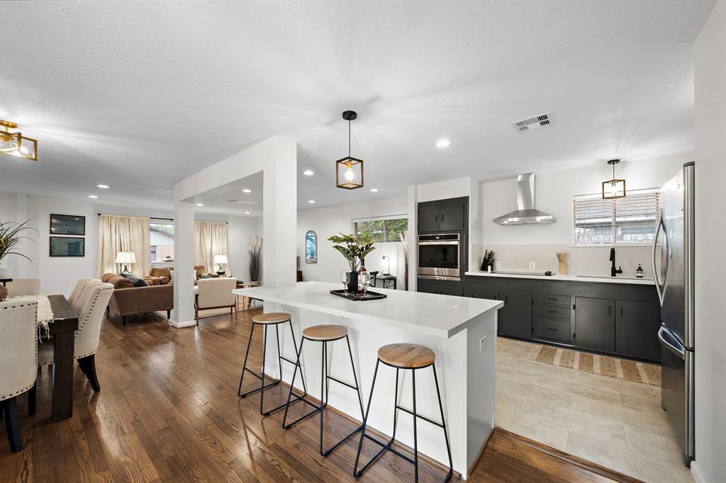a kitchen with stainless steel appliances kitchen island granite countertop a stove a refrigerator a kitchen island a dining table and chairs with wooden floor