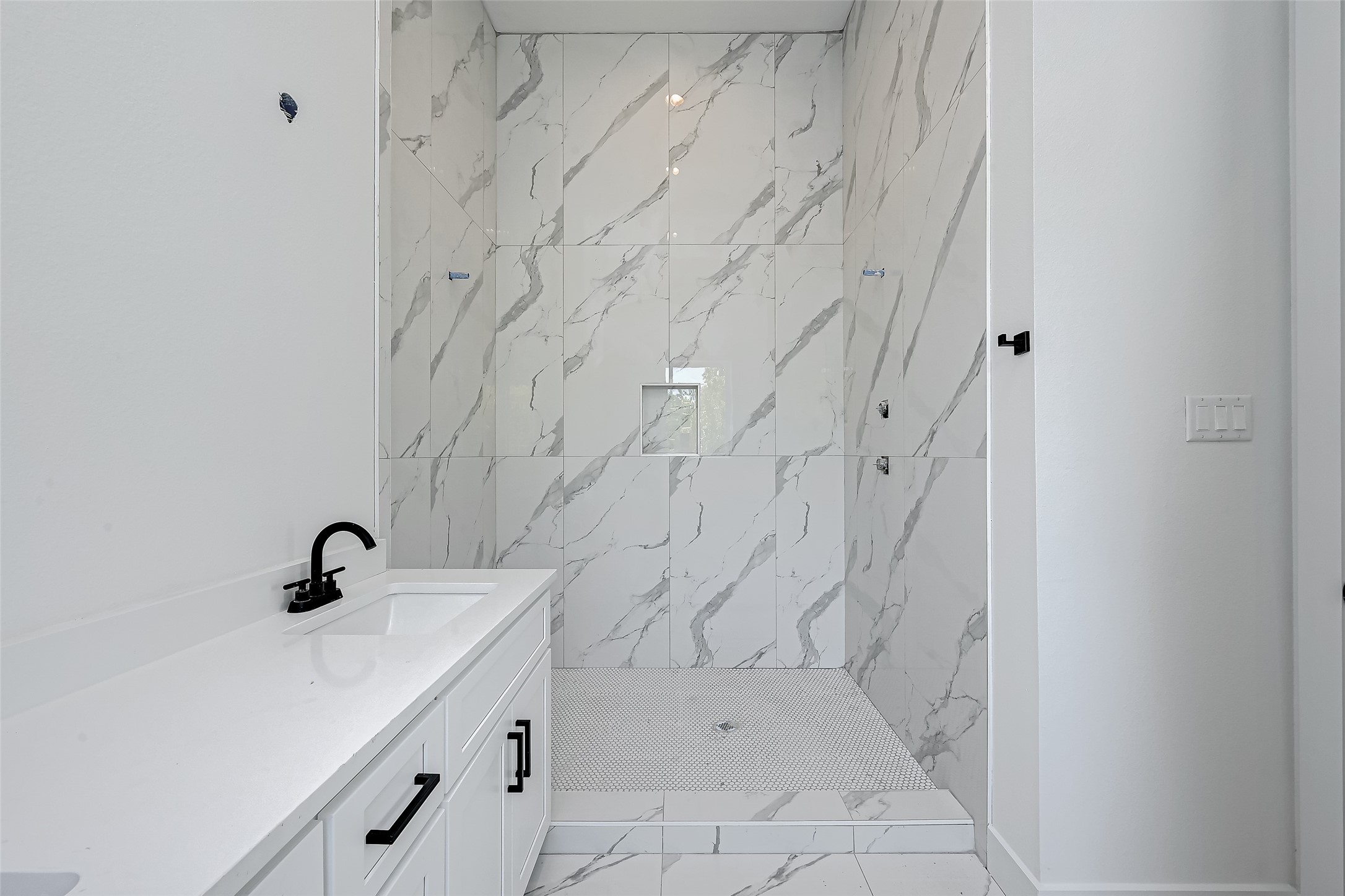 6032 Beall Street Houston, TX 77091 - Photo 19 of 26 The spa-inspired walk-in shower is wrapped in elegant porcelain tile with dramatic veining, offering a luxurious retreat in the primary en-suite bathroom.