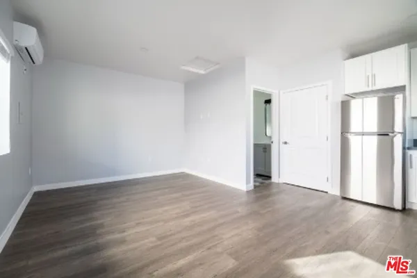a view of an empty room with wooden floor fridge and a window
