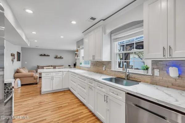 a kitchen with a sink dishwasher a stove and white cabinets with wooden floor