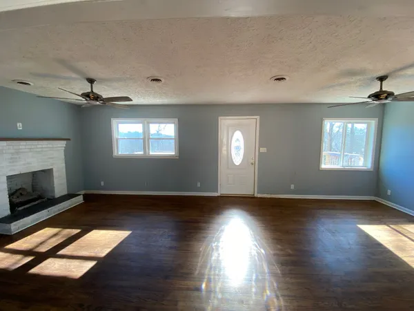 a view of an empty room with wooden floor fireplace and a window
