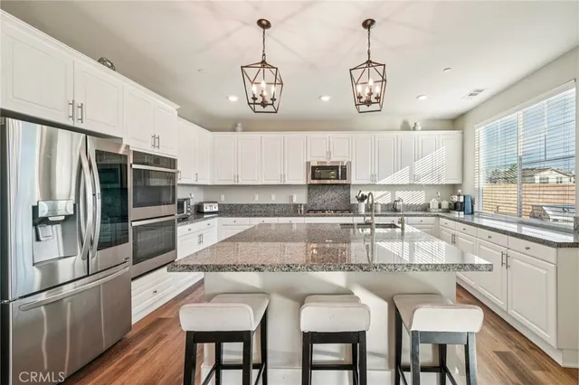 a kitchen with stainless steel appliances granite countertop a sink a stove a refrigerator cabinets and chairs