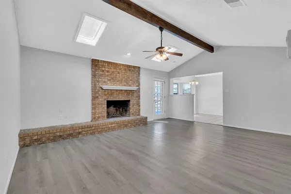 a view of an empty room with wooden floor fireplace and a window
