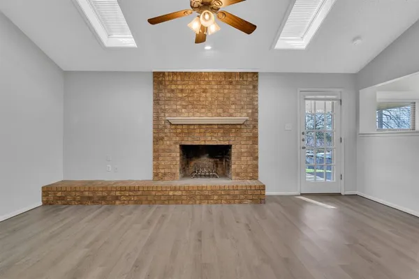 a view of an empty room with wooden floor fireplace and a window