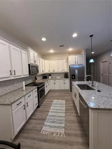 a large kitchen with stainless steel appliances granite countertop a stove a sink dishwasher a refrigerator and white cabinets with wooden floor