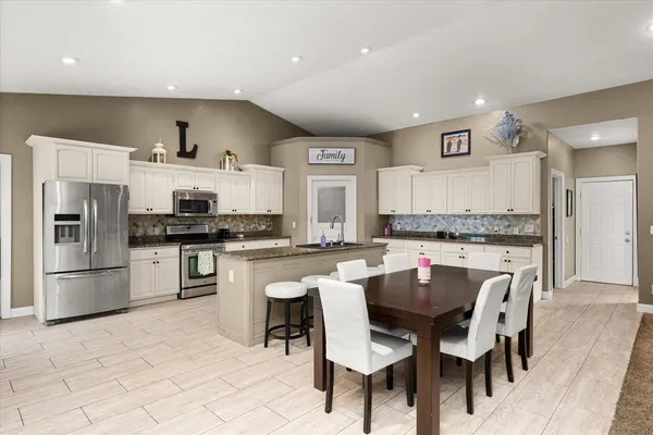 a kitchen with stainless steel appliances kitchen island granite countertop a table chairs sink and cabinets