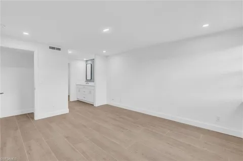 a view of an empty room with wooden floor and kitchen