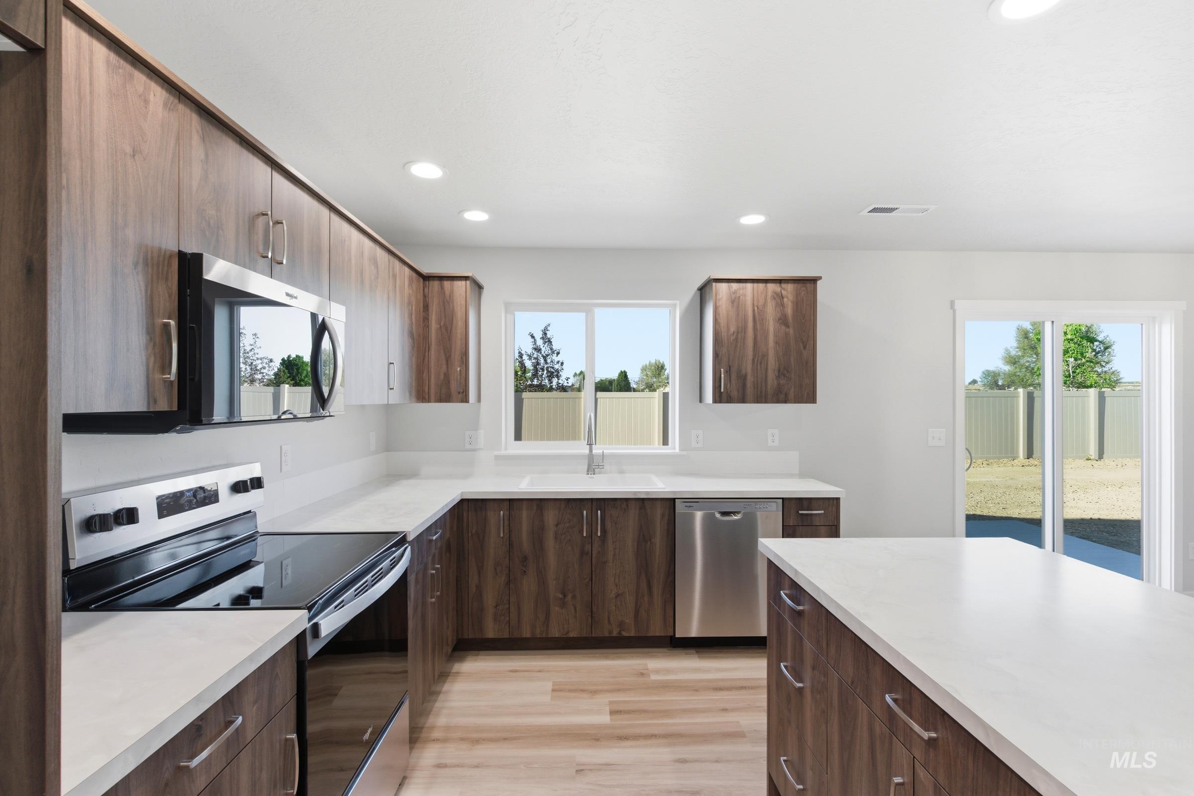 13709 Redway Court Caldwell, ID 83607 - Photo 4 of 28 Modern kitchen featuring wood-finish cabinetry, light-toned countertops, and stainless steel appliances including a built-in microwave, electric range, and dishwasher