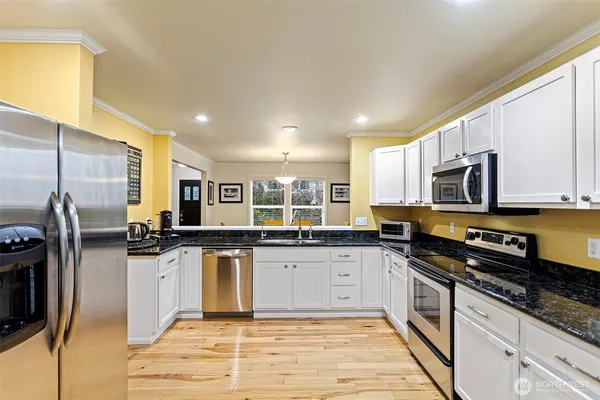 a kitchen with stainless steel appliances granite countertop a stove top oven a sink a refrigerator white cabinets and a granite counter top