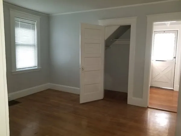 an empty room with wooden floor closet and windows