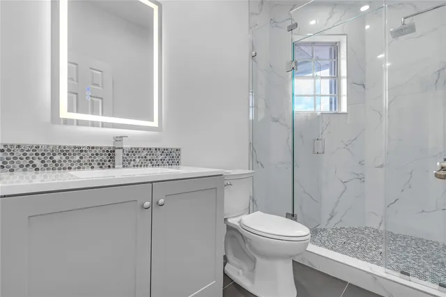 a bathroom with a granite countertop toilet a sink a mirror and shower