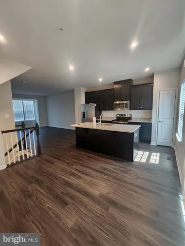 a kitchen with stainless steel appliances kitchen island granite countertop a refrigerator a stove and a wooden floors