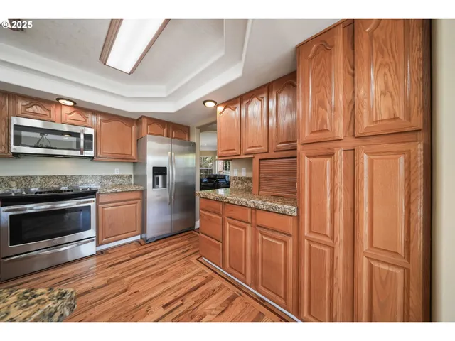 a kitchen with stainless steel appliances granite countertop a refrigerator oven a sink dishwasher and wooden cabinets with wooden floor