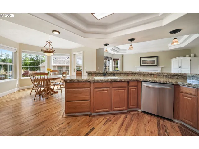 a kitchen with granite countertop a stove a sink dishwasher and a dining table with wooden floor