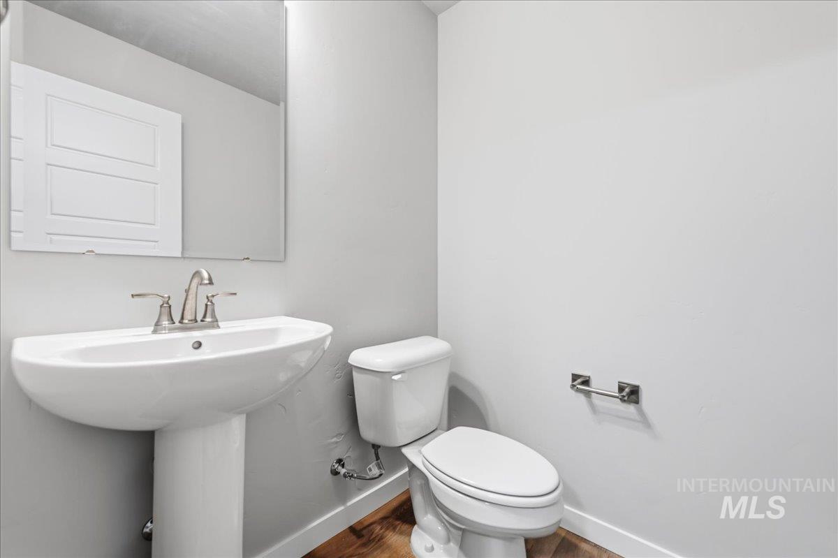 12475 West Victory Road Boise, ID 83709 - Photo 22 of 26 Pedestal sink with brushed nickel faucet, frameless mirror, white toilet, and wood-finish flooring