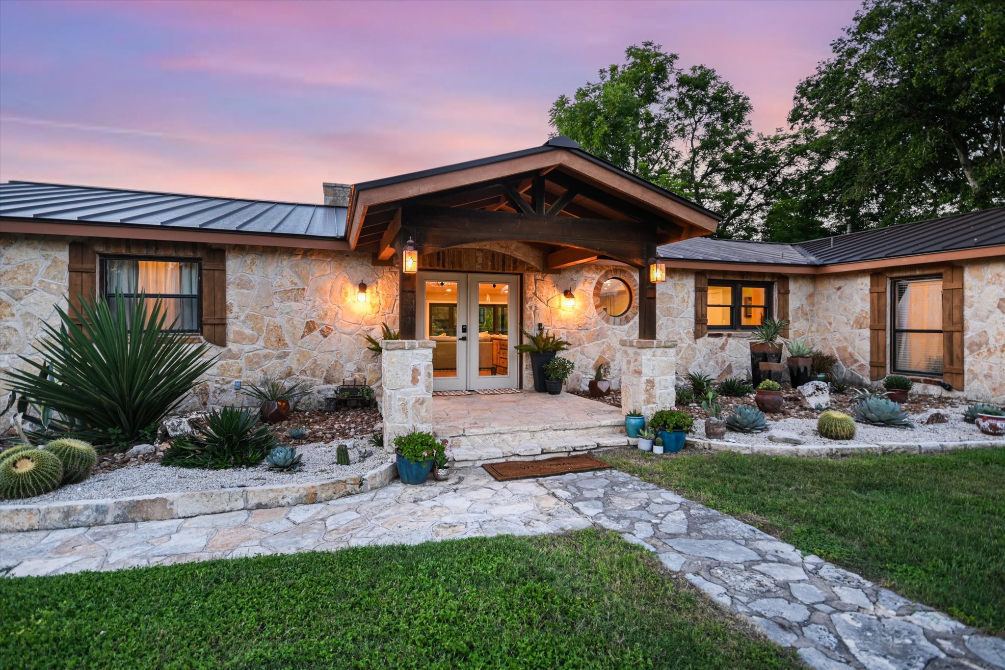 2411 Spoke Hollow Road Wimberley, TX 78676 - Photo 1 of 37 A stone-clad home welcomes with an inviting porch and meticulously landscaped desert-style gardens.