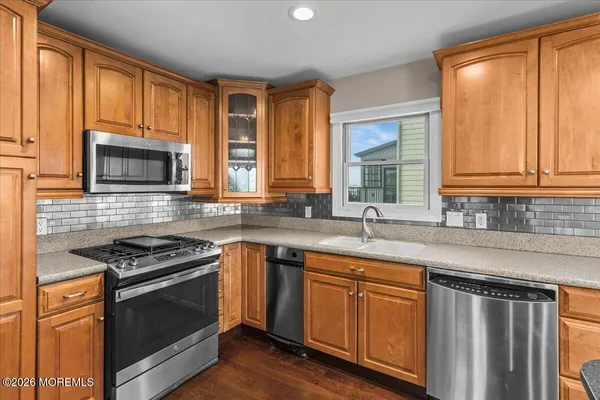 a open kitchen with stainless steel appliances granite countertop a stove top oven a sink a dining table and chairs with wooden floor