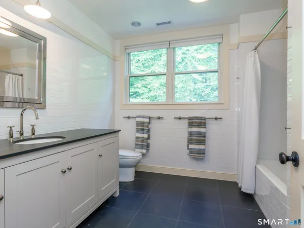 a bathroom with a granite countertop sink toilet a large mirror a bathtub and window