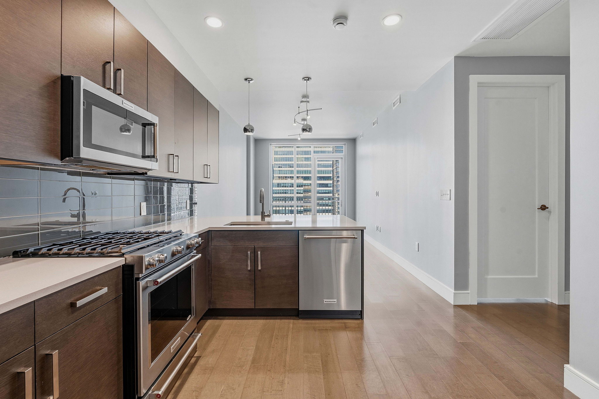 222 West Avenue, Unit 2207 Austin, TX 78701 - Photo 4 of 30 Modern kitchen featuring wood-finish cabinetry, stainless steel appliances, light-toned countertops, a tile backsplash, and recessed lighting