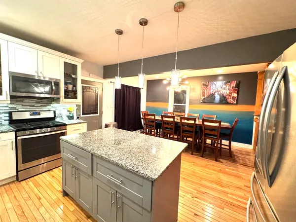 a kitchen with stainless steel appliances granite countertop a refrigerator a stove top oven a sink dishwasher and dining table with wooden floor