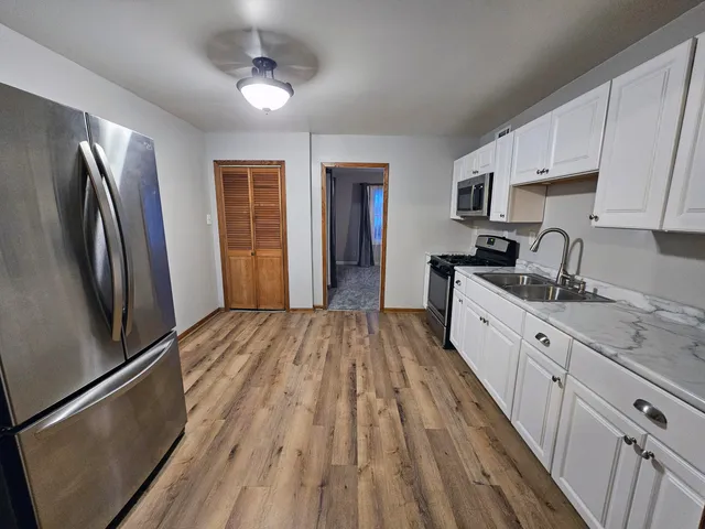 a kitchen with stainless steel appliances granite countertop a refrigerator oven a sink dishwasher and white cabinets with wooden floor