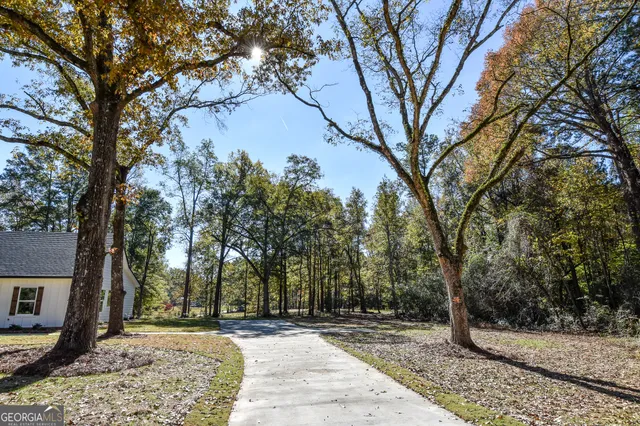 a view of a white house next to a yard with large trees