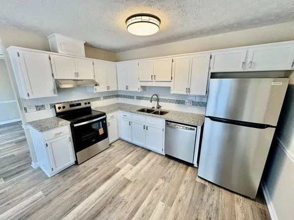 a kitchen with stainless steel appliances a refrigerator a stove a sink and white cabinets