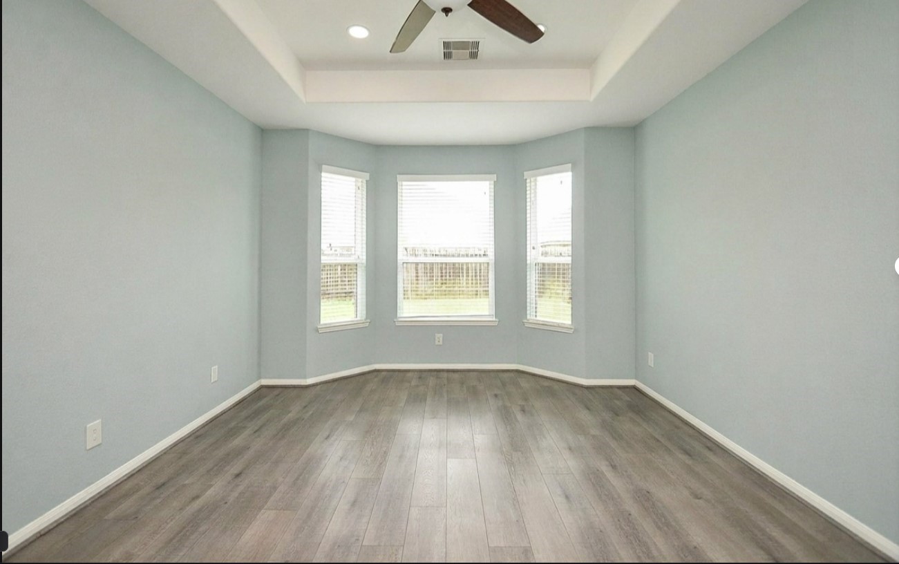 7042 Sliding Rock Circle Spring, TX 77379 - Photo 11 of 36 Spacious primary bedroom featuring elegant wood floors, abundant natural light from large bay windows, and a stylish tray ceiling with a fan.