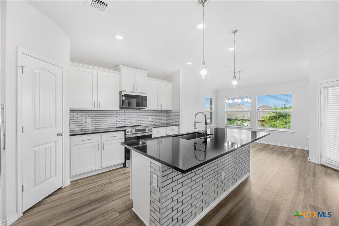 6166 Lavaca Drive Belton, TX 76513 - Photo 16 of 41 a kitchen with stainless steel appliances granite countertop a stove a sink dishwasher a microwave oven and a dining table with wooden floor