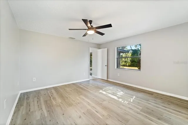an empty room with wooden floor ceiling fan and windows