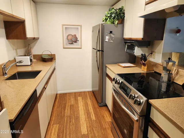 a kitchen with stainless steel appliances granite countertop a refrigerator a stove and a sink with wooden floor