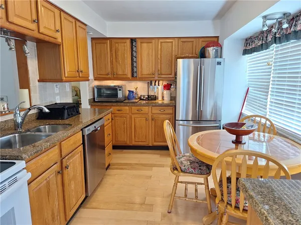 a kitchen with stainless steel appliances granite countertop a refrigerator a stove top oven a sink dishwasher and dining table with wooden floor
