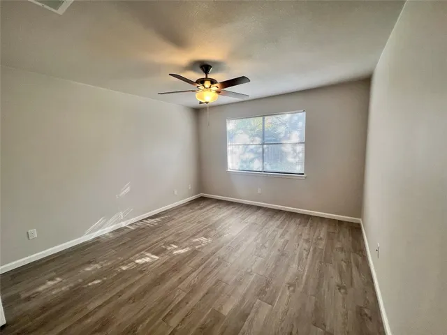 an empty room with wooden floor chandelier fan and windows