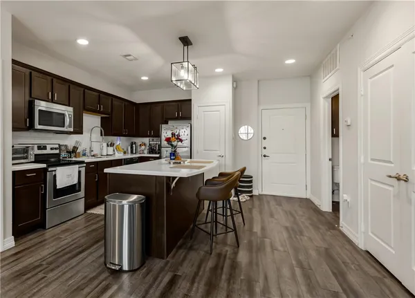 a kitchen with stainless steel appliances granite countertop a refrigerator a stove top oven a sink dishwasher a dining table and chairs with wooden floor