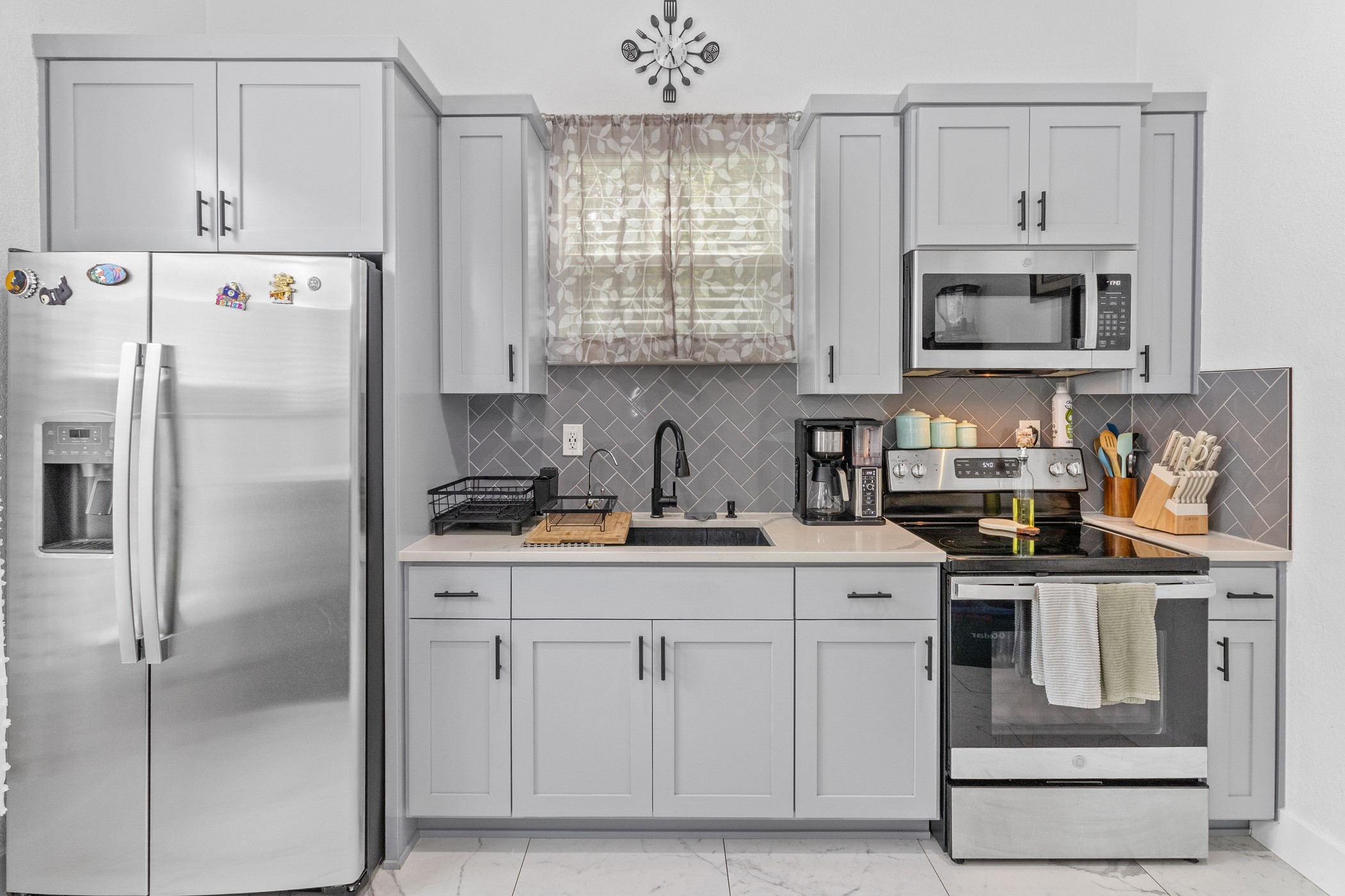 123 Zacate Street Elgin, TX 78621 - Photo 9 of 33 Modern kitchen featuring light gray shaker-style cabinetry with matte black hardware, a stainless steel side-by-side refrigerator, and a coordinating stainless steel range with overhead microwave