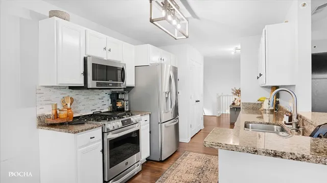 a kitchen with stainless steel appliances granite countertop a stove a sink dishwasher a refrigerator and a microwave with wooden floor