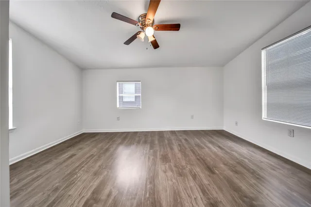 an empty room with wooden floor fan and windows