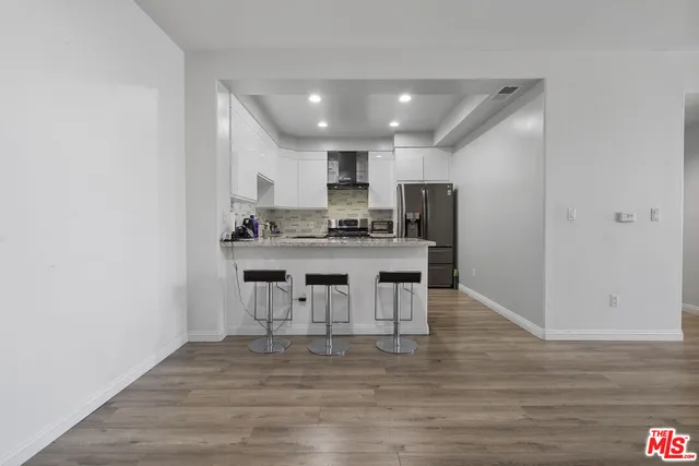 a view of a dining room with kitchen island stainless steel appliances a sink and wooden floor