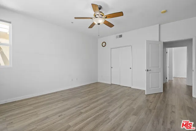 a view of an empty room with window a ceiling fan and wooden floor