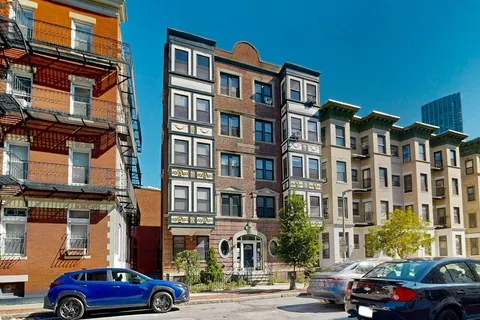 a front view of a building with lot of cars and trees