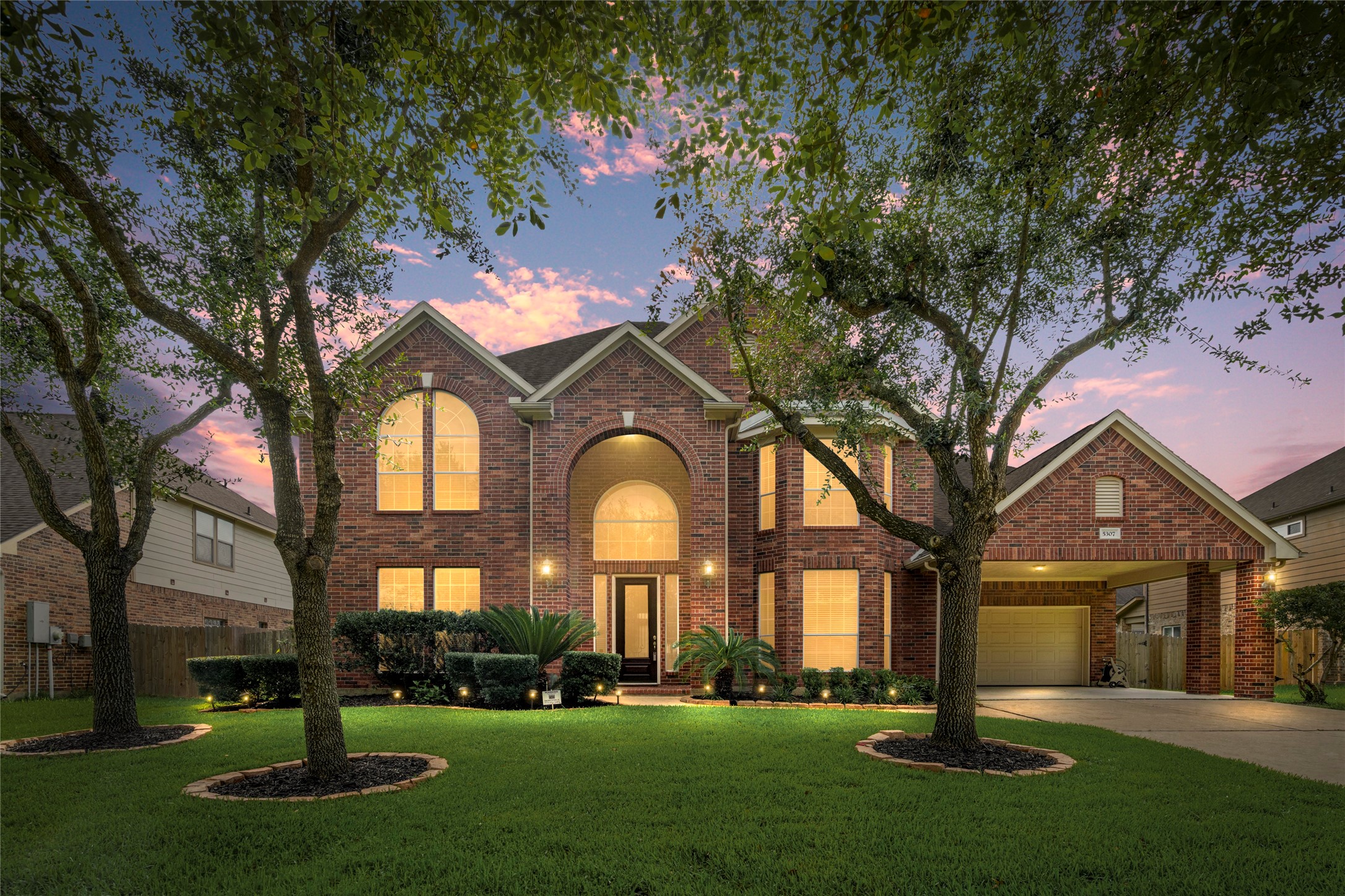 Twilight settles softly over this stunning all-brick estate in the gated Savannah Landings community, where soaring arched windows and timeless brick craftsmanship are framed by mature trees and a brilliant Texas sunset, a true showstopper from the curb.