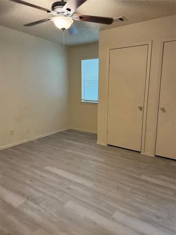 an empty room with wooden floor fan and windows