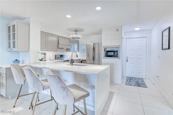 a kitchen with stainless steel appliances a sink a stove a refrigerator cabinets and chairs