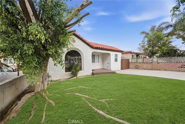 a view of a white house with a big yard plants and large trees