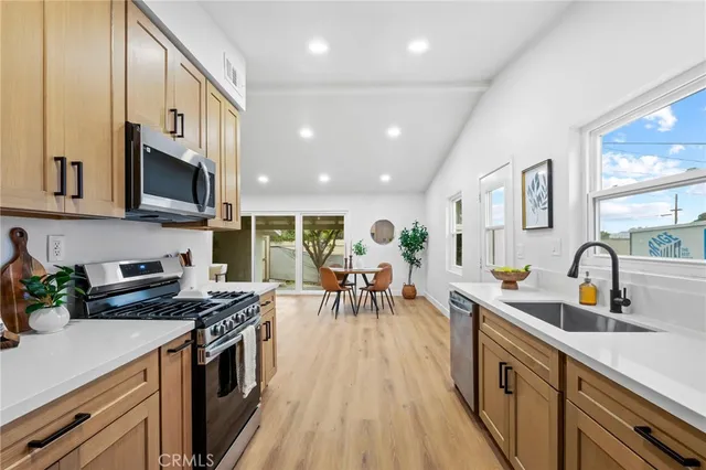 a kitchen with stainless steel appliances a stove a sink a oven a dining table and chairs with wooden floor