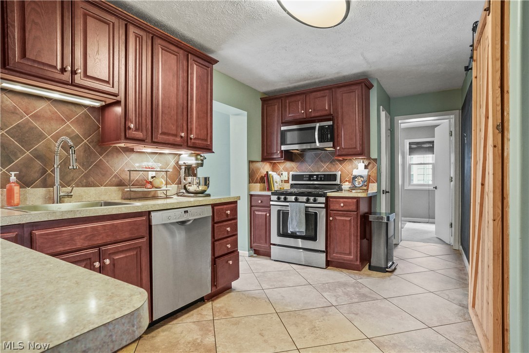 2122 Campus Road Cleveland, OH 44121 - Photo 13 of 39 Kitchen with stainless steel appliances, sink, light tile flooring, and backsplash