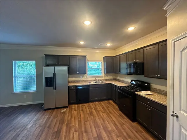 a kitchen with stainless steel appliances granite countertop a refrigerator a sink dishwasher a stove and a microwave oven on wooden floor